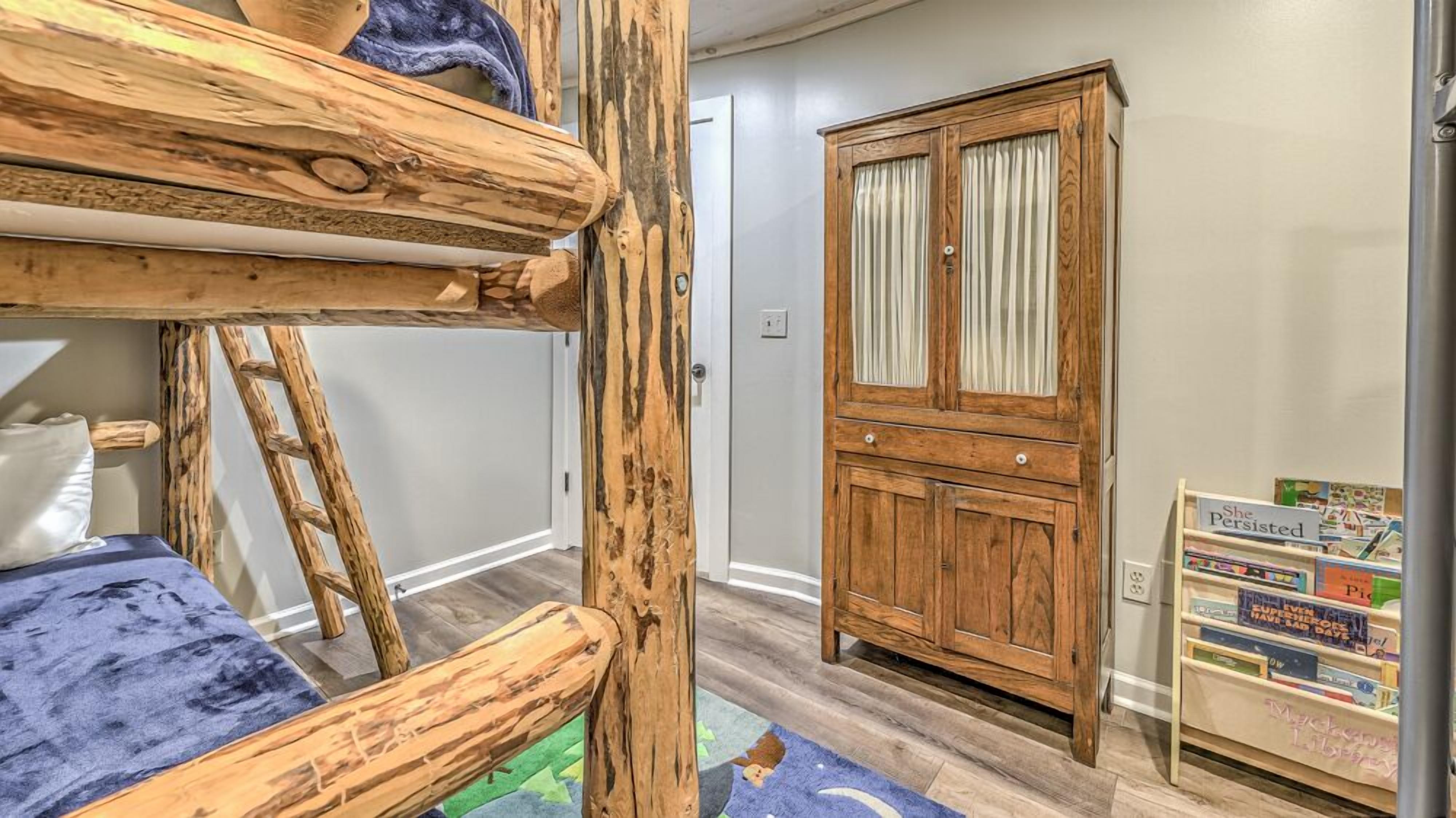 A bunk bed with a ladder, a wooden wardrobe, and a bookshelf with children's books.
