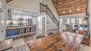 A spacious kitchen with a central island, a dining area with a large wooden table, and a staircase leading to an upper level. - Lake Cove Oasis - Waterfront on Lake Blue Ridge | Private Yard and Dock | Pet Friendly (Morganton)
