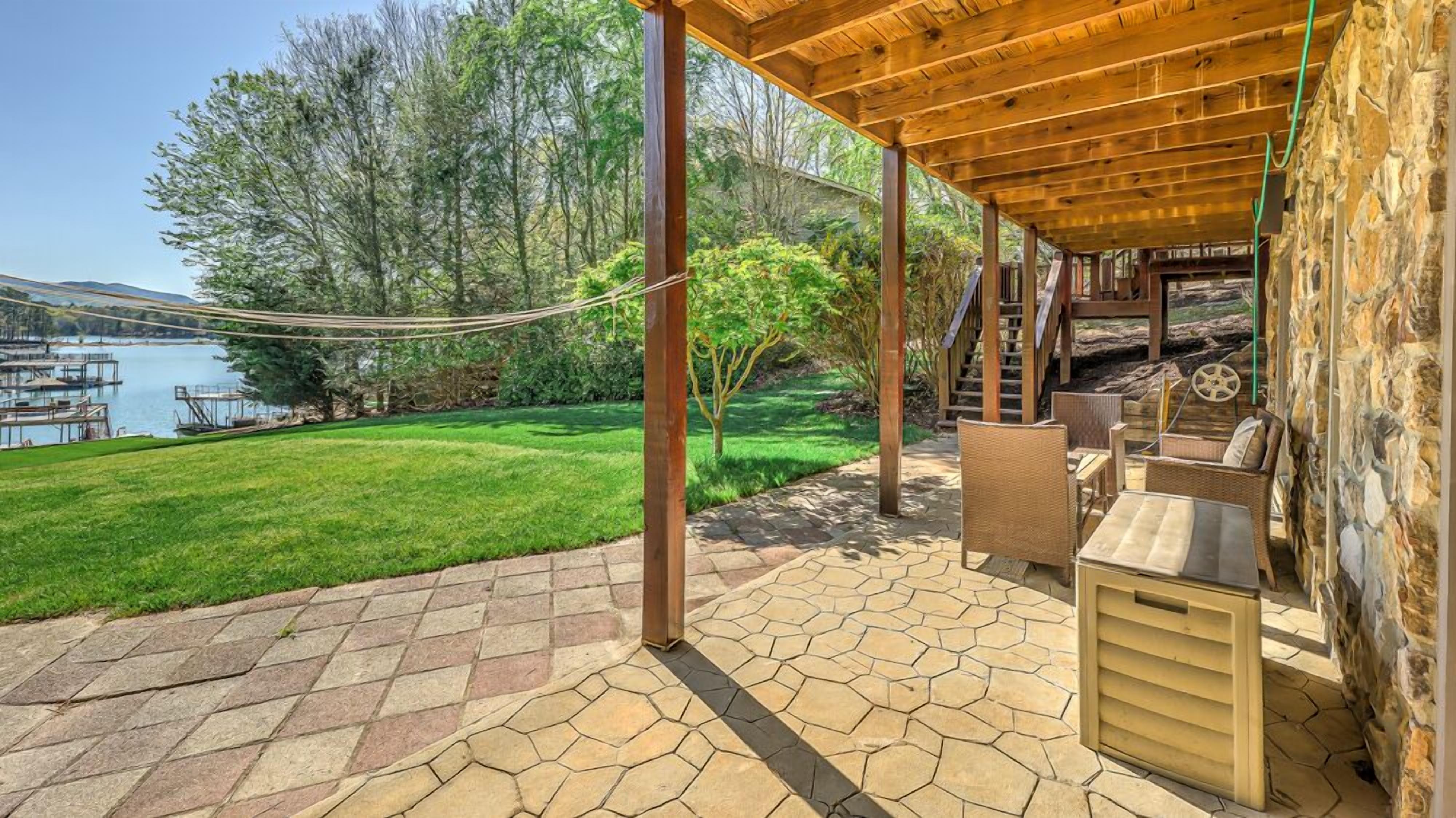 A covered patio with stone flooring, wicker furniture, and a view of a lake and trees.