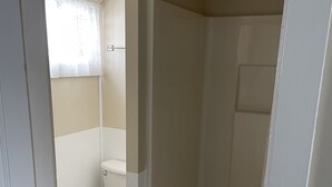 A bathroom with a toilet, a shower stall, and a window with a curtain. - Autrain Motel (Au Train)
