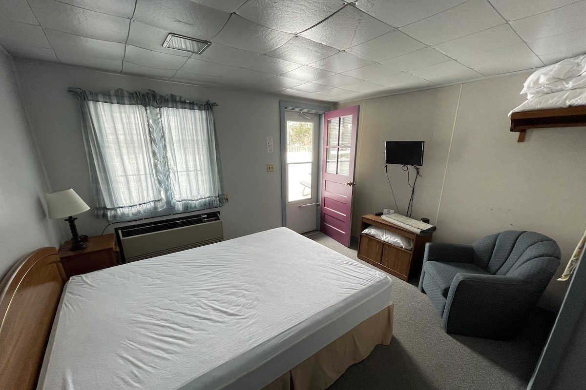 Quarto de hotel com cama, escrivaninha, cadeira, televisão e janela com cortinas.