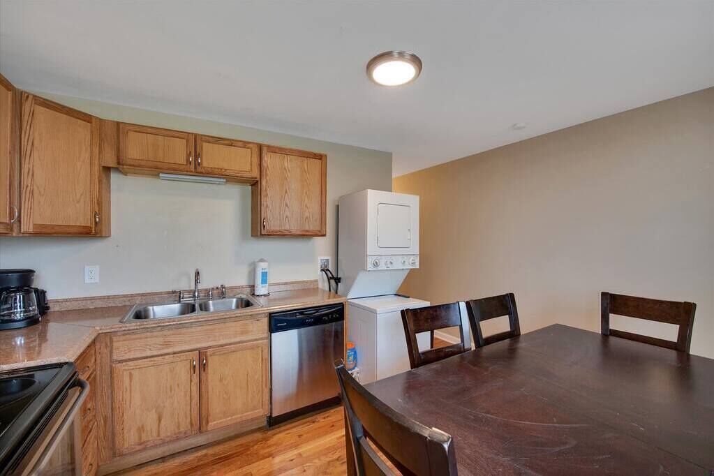 Una cocina compacta con armarios de madera, lavavajillas, refrigerador blanco y una mesa de comedor con sillas.