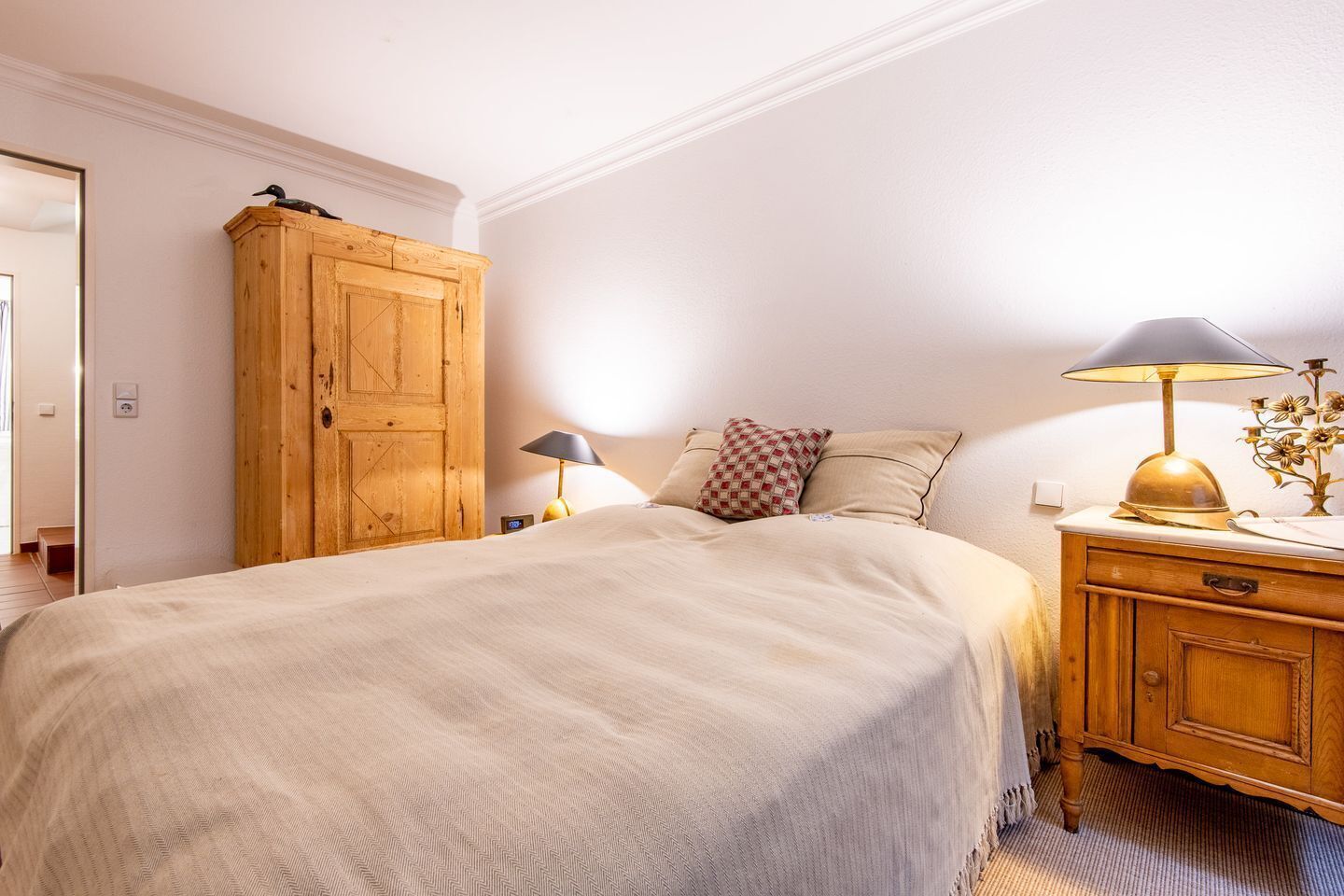 A bedroom with a large bed, wooden wardrobe, bedside lamps, and a nightstand.