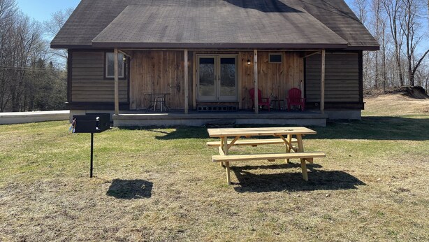 A wooden cabin with a porch, two red Adirondack chairs, and a picnic table. - Woof Pack Shack  #3 (West Leyden)