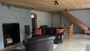 A spacious living room with a fireplace, a sofa, and a dining area with wooden chairs and a table. - Woof Pack Shack  #3 (West Leyden)