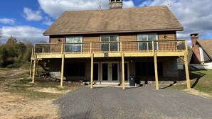 A two-story house with a wooden deck and a chimney. - Woof Pack Shack  #3 (West Leyden)