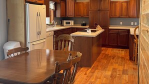 A kitchen with wooden cabinets, a refrigerator, a microwave, and a dining table with chairs. - Woof Pack Shack  #3 (West Leyden)