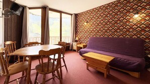 Una habitación con una mesa de comedor de madera, sillas, un sofá morado, un banco de madera, un televisor montado en la pared y un papel tapiz estampado.