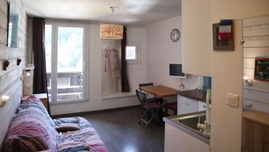 Une pièce confortable comprenant un lit, une table à manger avec des chaises, un petit coin cuisine et une fenêtre avec des rideaux.