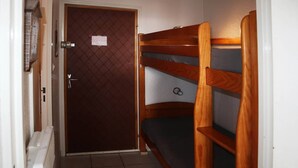 Een smalle gang met een bruine deur, een radiator en een stapelbed met een matras.