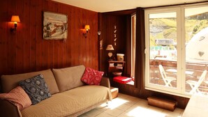 Een knus interieur met een houten wand, een bank met kussens, een raam met uitzicht op het exterieur en een wandlamp.