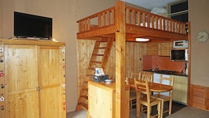 Habitació d'estil cabana acollidora amb un llit superposat, una cuina americana petita, zona de menjador i televisió.