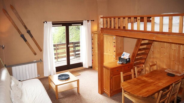 Habitació acollidora amb una lliteràs, una taula petita amb un plat, una cadira i una finestra amb cortines.