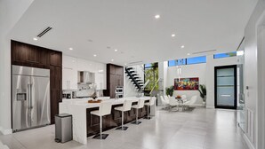 Uma cozinha moderna com ilha central, eletrodomésticos de aço inoxidável e uma escada que leva a um andar superior.