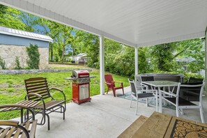 A covered patio with outdoor furniture, a grill, and a view of a backyard with a stone wall and greenery. - Short Walk to Downtown Branson & Branson Landing with Private Hot Tub & Free Tickets (Branson)