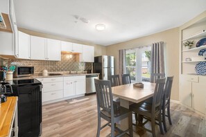 A modern kitchen with white cabinets, a stainless steel refrigerator, and a dining area with a wooden table and chairs.