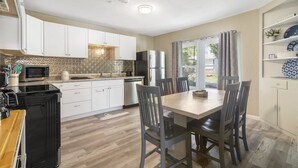 Una cocina moderna con armarios blancos, un refrigerador negro, un microondas y una zona de comedor con una mesa y sillas de madera.
