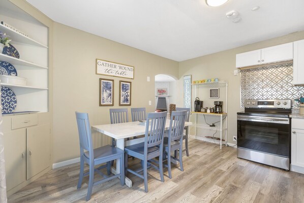 A kitchen with a dining table and chairs, a coffee machine, and a stove.