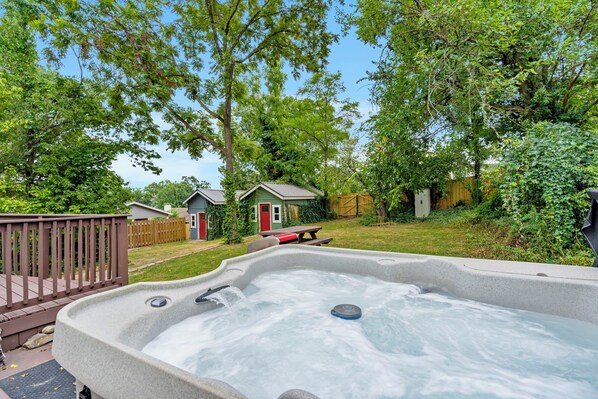 A hot tub in a backyard with a wooden deck, a small shed, and a wooden fence.