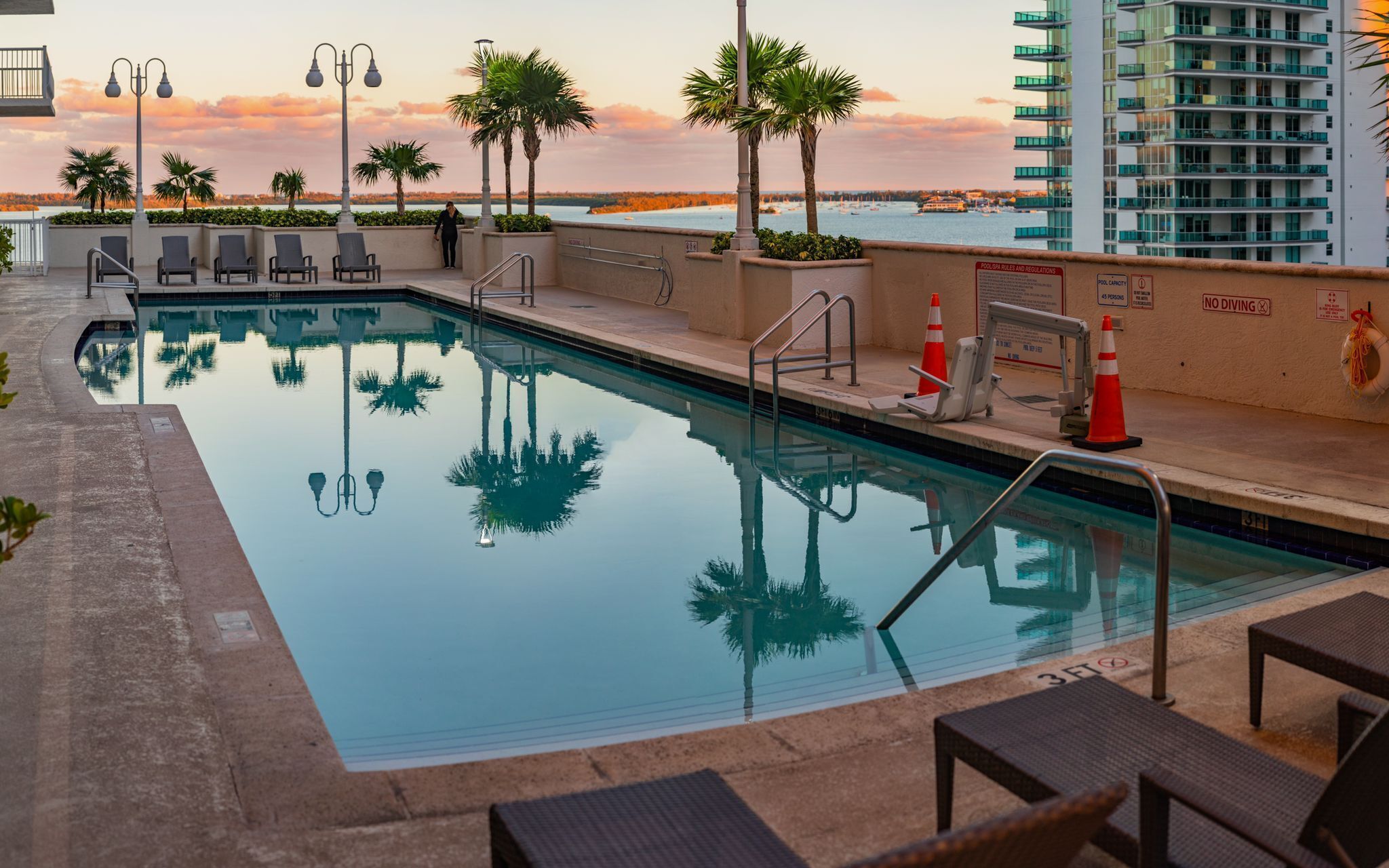 Una piscina con sillones de descanso y vista al océano al atardecer.