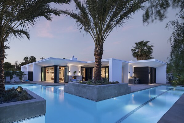 Une maison moderne dotée d’une piscine, de grandes fenêtres et d’un espace extérieur bien éclairé.