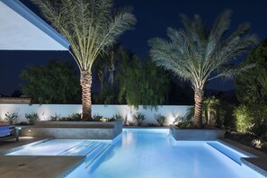 Une piscine au design moderne, entourée de palmiers et agrémentée d’un aménagement paysager soigné.