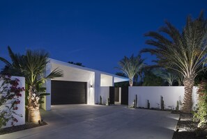 Une maison moderne dotée d’un grand garage, de palmiers et d’un jardin bien entretenu.
