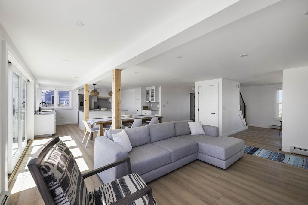 A spacious living area with a gray sectional sofa, a dining table, and a kitchen in the background.