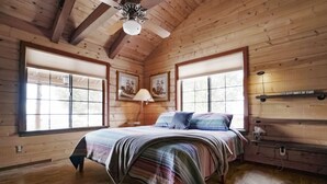 A wooden cabin bedroom with a bed, two windows, a ceiling fan, and a wall-mounted shelf. - Private Sauna and Stunning Views of Mesa Verde, Walk to Mancos State Park (Mancos)