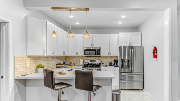 A modern kitchen with white cabinets, stainless steel appliances, and pendant lighting. - Modern 2BHK - 15 mins bus ride to Time Square, NYC (West New York)