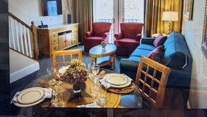 A living room with a sofa, armchairs, a dining table set with plates and glasses, a small table with a vase, and a television on the wall. - Luxury Resort with Restaurants , 5 minutes to the beach (West Yarmouth)