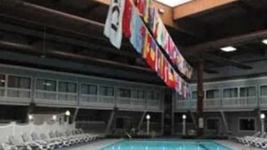 An indoor swimming pool with a ceiling adorned with flags, lounge chairs, and a poolside area. - Luxury Resort with Restaurants , 5 minutes to the beach (West Yarmouth)
