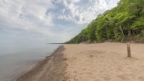 A beach with a pebbly shoreline, a sandy area, and a forested hillside.
