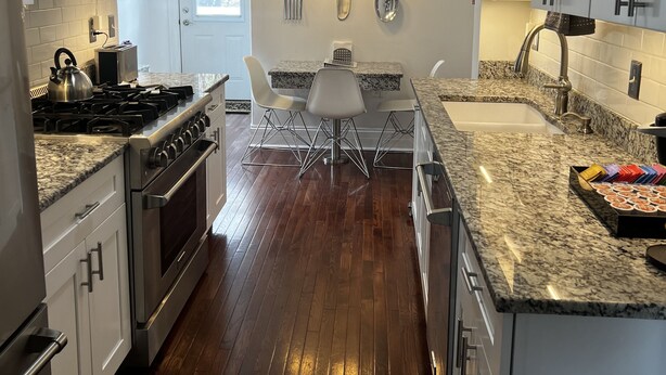 A modern kitchen with white cabinets, a granite countertop, stainless steel appliances, and a dining area with a table and chairs. - Historic three-level home in the Highlands (Louisville)