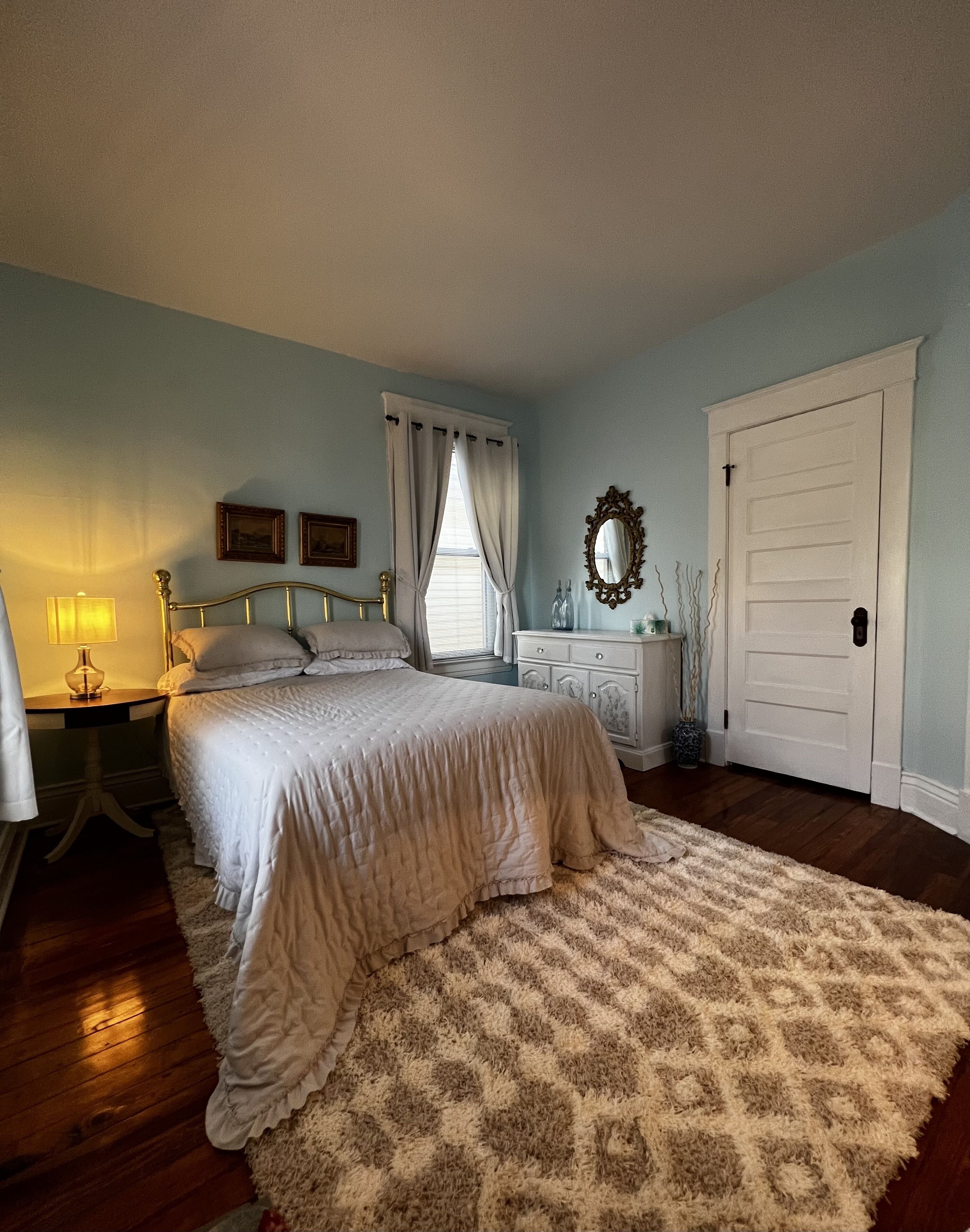A bedroom with a bed, nightstands, a dresser, a mirror, and a door.
