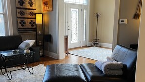 A spacious living room with a black leather sofa, a glass coffee table, and a large rug. A wall-mounted skull decoration and a lamp are visible. - Historic three-level home in the Highlands (Louisville)
