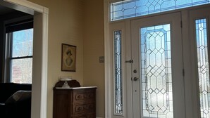 A room with a chandelier, a wooden dresser, a framed picture, and a large window with stained glass. - Historic three-level home in the Highlands (Louisville)
