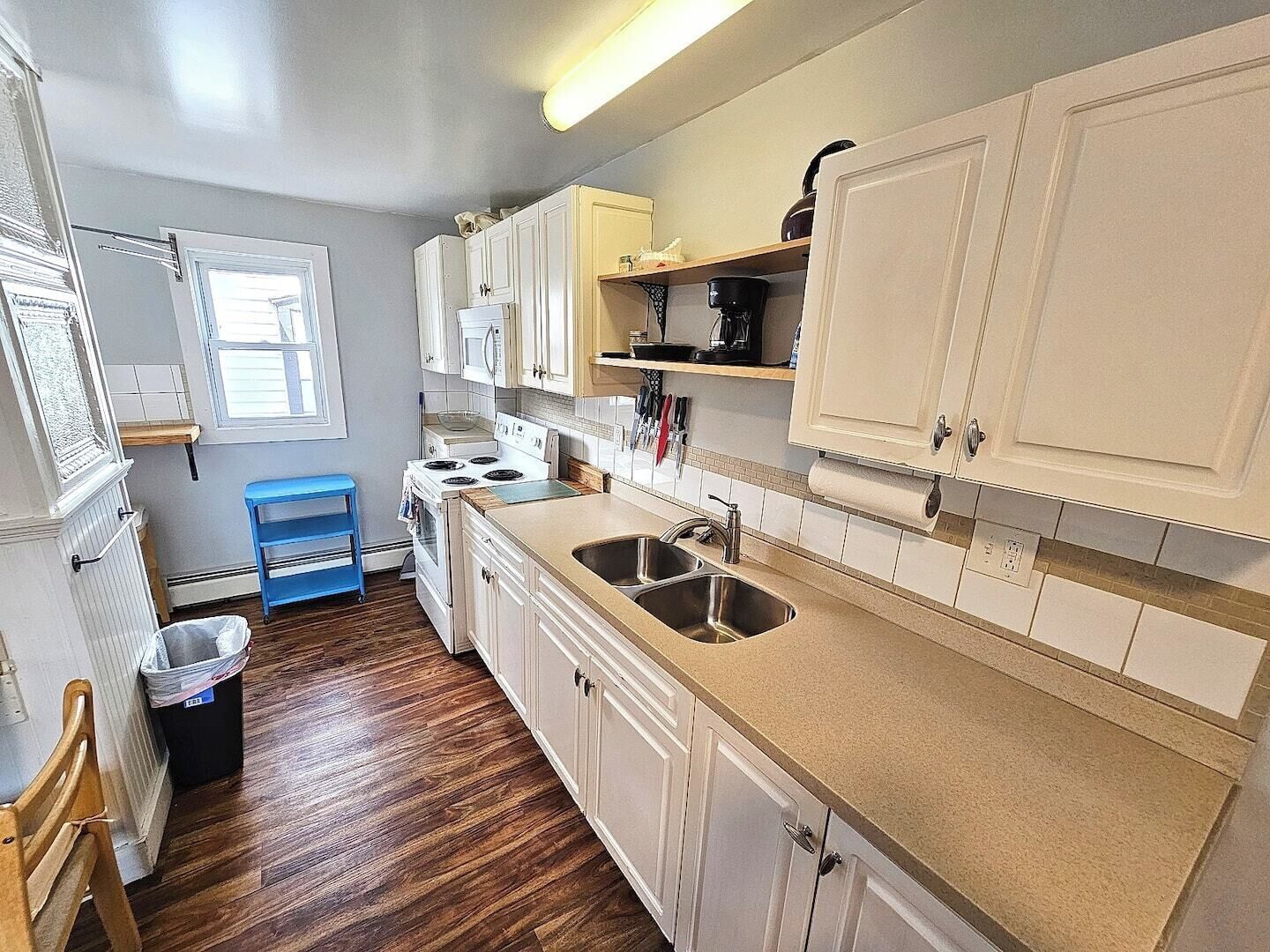 A kitchen with white cabinets, a blue stool, a stove, and a sink.