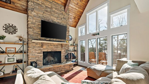 Una sala de estar acogedora con chimenea de piedra, televisor de pantalla plana montado encima y un ventanal con vistas al exterior.