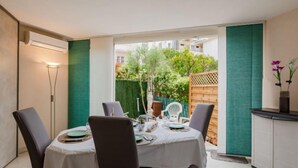 A dining area with a table set for two, chairs, a small cabinet, and a view of a garden. - Le chant de la mer by Interhome (Fréjus)