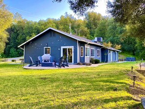 A blue house with a patio, outdoor seating, and a small shed in a grassy yard.