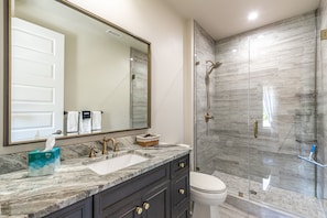 A modern bathroom with a marble sink, a large mirror, a glass shower enclosure, and a toilet.