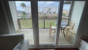 Un balcon doté d’une terrasse en bois, d’une table avec des chaises et offrant une vue sur les immeubles et les palmiers.