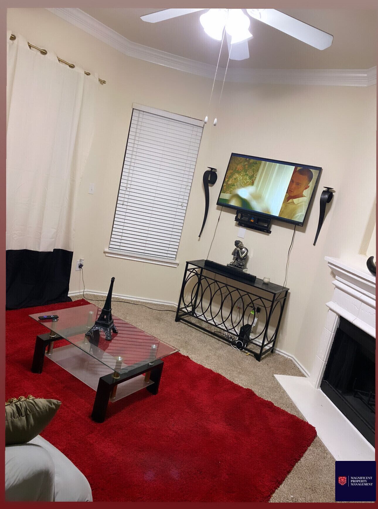 A living room with a television, a fireplace, a glass coffee table, and a red carpet.