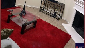 Een woonkamer met een televisie, een open haard, een glazen salontafel en een rood tapijt.
