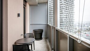 Un balcón con una pequeña mesa y sillas, una planta en maceta y vistas de un edificio de gran altura.