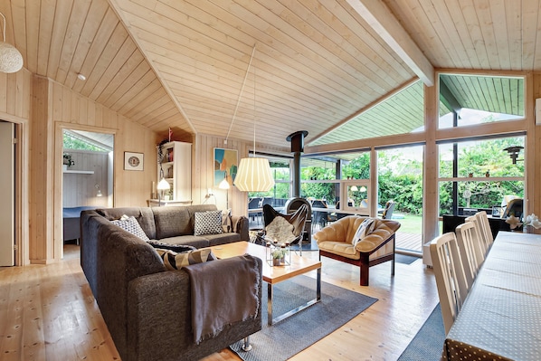 A spacious living area with a wooden ceiling, large windows, and a mix of seating arrangements including sofas and chairs.