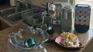A kitchen with a sink, a coffee maker, a tea kettle, and a coffee machine. There are also some food packets and a glass bowl on the counter. - Beautiful Ocean view of Sunny South Shore at Poipu Beach in Kauai (Koloa)