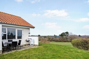 A house with a tiled roof, a patio with a table and chairs, and a grassy yard.