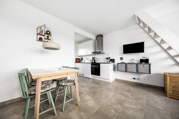 A modern kitchen with white cabinetry, a built-in oven, and a dining area with a wooden table and chairs.